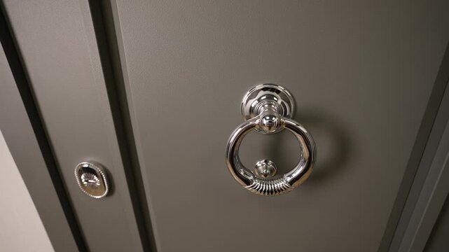 Gray residential front door featuring a sleek chrome ring door knocker and security peephole, representing home security and welcoming