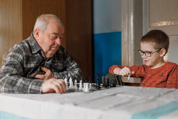 A grandfather and boy smile during chess. The concept shows family bonding and joyful learning. © Natallia