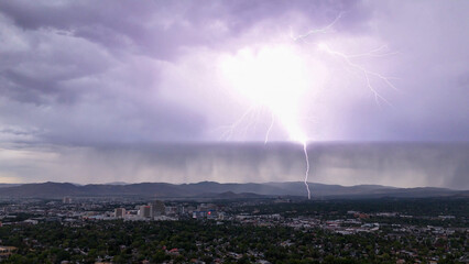 Aerial view of an electrifying storm unleashing a dramatic lightning strike over the cityscape under a heavy, rain-laden sky, Reno, Nevada, United States.
