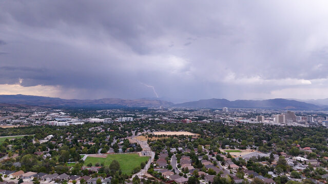Aerial view of a sudden lightning strike over the cityscape, with dramatic contrasts between the dark storm clouds and the bright urban landscape, Reno, Nevada, United States.