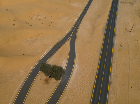 Aerial view of a stark contrast where smooth asphalt ribbons cut through the undulating textures of the sandy desert, punctuated by a small patch of green, Dubai, Dubai, United Arab Emirates.