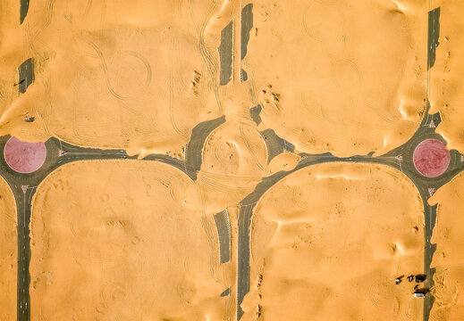 Aerial view of geometric patterns etched in the golden desert sand, punctuated by vibrant red circles, Dubai, Dubai, United Arab Emirates.
