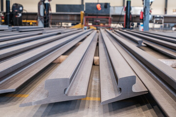 Steel railway rails stacked in industrial workshop, close-up of metal production and manufacturing process in factory environment