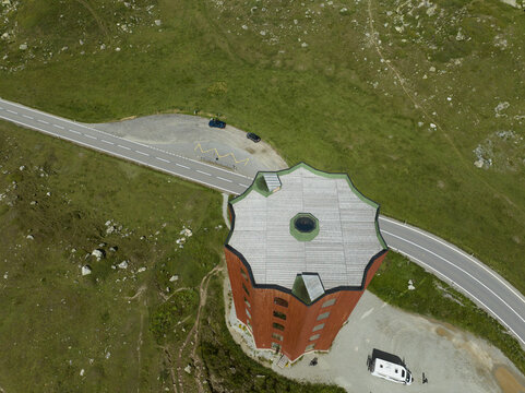 Aerial view of the striking red and gray tower contrasting with the vivid green landscape, bisected by winding roads, Julier Pass, Grisons, Switzerland.