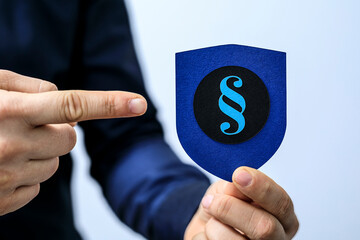 Hand points to a blue shield with a paragraph symbol, representing legal protection and security.