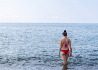 Attractive woman with long hair, wearing red bikini entering the sea. Activity