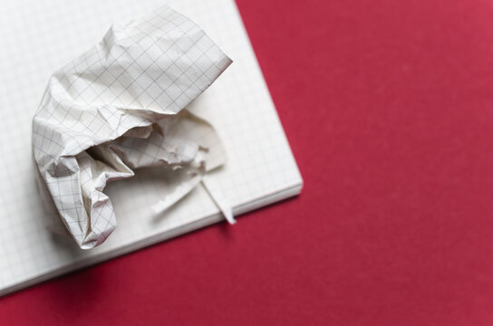 folgio di carta a quadretti stropicciato sopra un blocco di fogli e una superfice di colore rosso con spazio vuoto