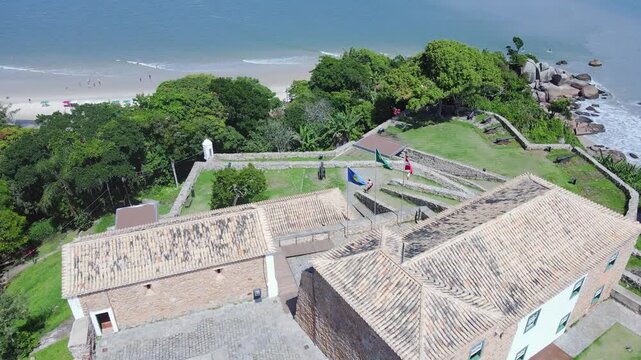 Aerial drone shot of the S&atilde;o Jos&eacute; da Ponta Grossa Fortress in front of Praia do Forte and Jurer&ecirc; Internacional beach, Florian&oacute;polis, Santa Catarina, large stone walls and 18th century cannons
