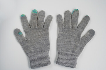 Pair of grey knitted fabric gloves with colorful visible mending on fingertips, representing sustainable fashion, clothing repair, and frugal living. Concept of reuse, recycling