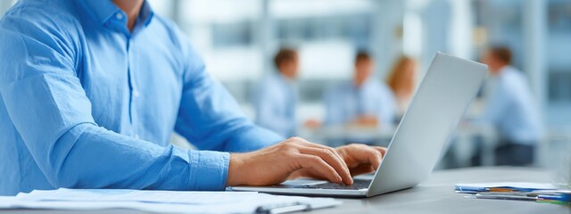 Close-up of businessman at desk with charts and laptop, blurred colleagues in background, representing corporate teamwork and data analysis.