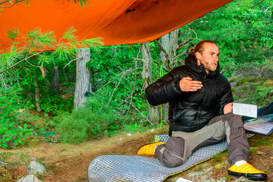 Outdoor adventure guide, young man with notebook, briefing group under tarp in boreal forest room for text shot on Georgian Bay in fall