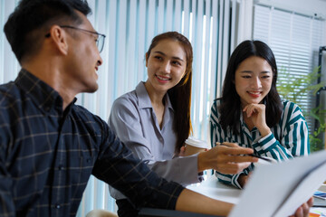 Three people are sitting at a table with a whiteboard behind them. One of the people is holding a pen and looking at a diagram on the board. Scene is focused and serious
