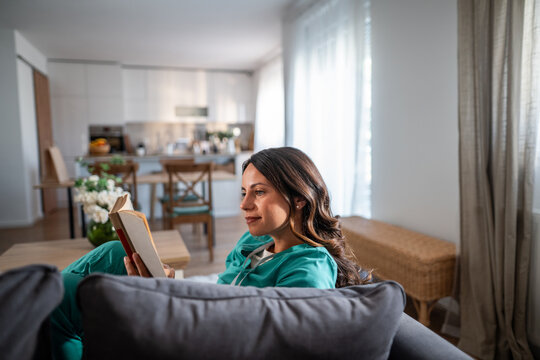 Woman doctor reading book relaxing on sofa at