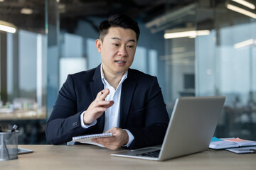 Young Asian businessman holding an online conference in the office, taking notes in a notebook