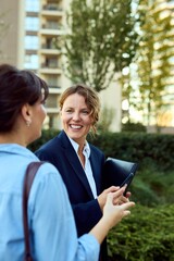 Obraz premium Business Women Chat Outdoors With Tablet In Office-Style Attire, Positive Professional Interaction