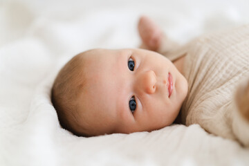 Cute baby lying on a soft white blanket with a calm expression while raising arms. Beautiful portrait of a child. Newborn baby lying on bed