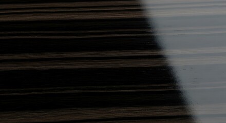 Close-up of a dark, glossy surface with parallel lines, illuminated by a bright light source creating a reflective area