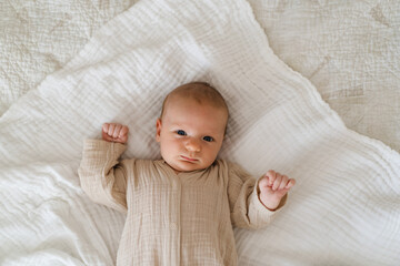 Cute baby lying on a soft white blanket with a calm expression while raising arms. Beautiful portrait of a child. Newborn baby lying on bed