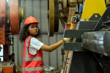 A female worker in a steel factory is operating machinery. A woman is focused working on a machine in a factory.