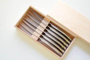 Steak knives in a wooden box on white background seen  from directly  above 