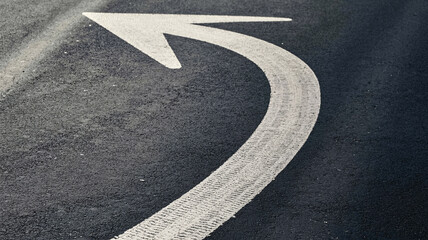 Dynamic white arrow marking curves on dark asphalt road surface, guiding direction forward