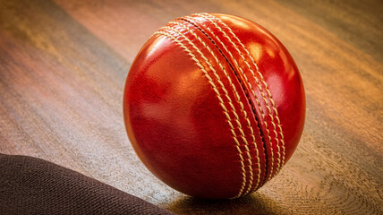 Vibrant red leather cricket ball with prominent stitching resting on a textured wooden surface, capturing intense sporting action and tradition.