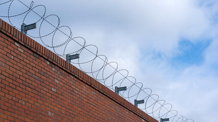 Strong brick wall topped with menacing barbed wire under a dramatic cloudy sky creating a sense of security and confinement