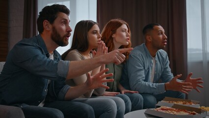 Happy concentrated four multiethnic friends supporting television sport team interested waiting result men women at home party watching tv football fans spectators soccer game on couch sofa together