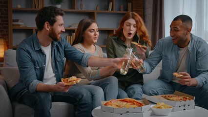 Happy multiracial four friends home party clinking bottles beer alcohol eating pizza on couch diversity buddies cheers with drinks talking communicate friendship birthday event celebration men women