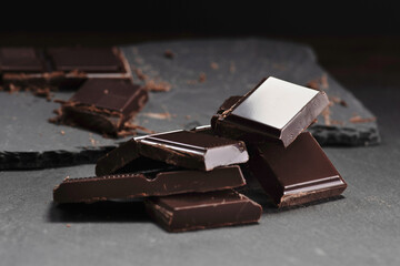 Broken dark chocolate and cocoa powder on a dark table