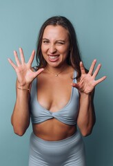 Woman in activewear making a playful gesture against blue background.