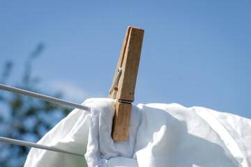 Laundry wooden clothes pin on white duvet cover against blue sky 