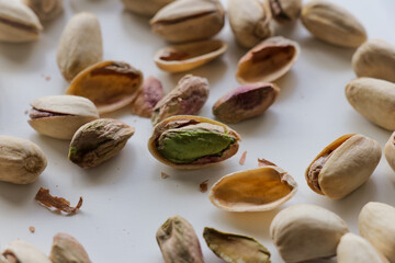 Peeled and whole pistachio nuts arranged together on clean white backdrop.