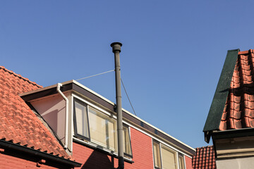 Chimney pipe on tiled roof, heating system exterior. Metal chimney pipe on red roof tiles, ventilation detail.