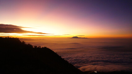 Vibrant sunrise over a sea of clouds from a mountain peak, with distant peaks emerging from the...