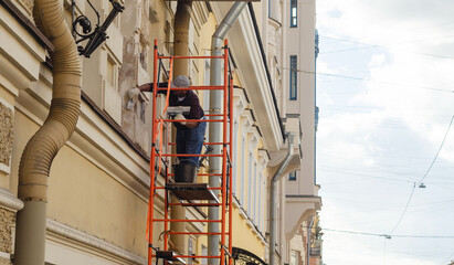 a female painter putties the facade of a house on scaffolding. © Andre_Dechapelle