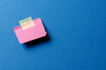 Piece of pink paper note with rough texture edges and adhesive tape with copy space for text on blue background
