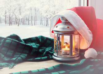 Christmas and New Year winter background-lantern with candle and Santa hat on the windowsill and winter nature outdoors