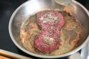 Frying pan with beef steak being cooked at home