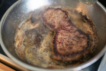 Frying pan with beef steak being cooked at home