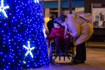 Happy child with disability admiring christmas tree lights with mother at night