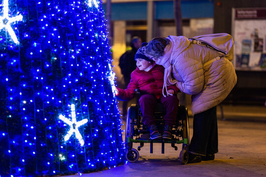Happy child with disability admiring christmas tree lights with mother at night