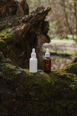 A dark and light glass serum bottle with a dropper, tree bark wood, moss. forest on a sunny day nature background. Concept of skin care, hydration, cosmetic demonstration eco-friendly product mock up