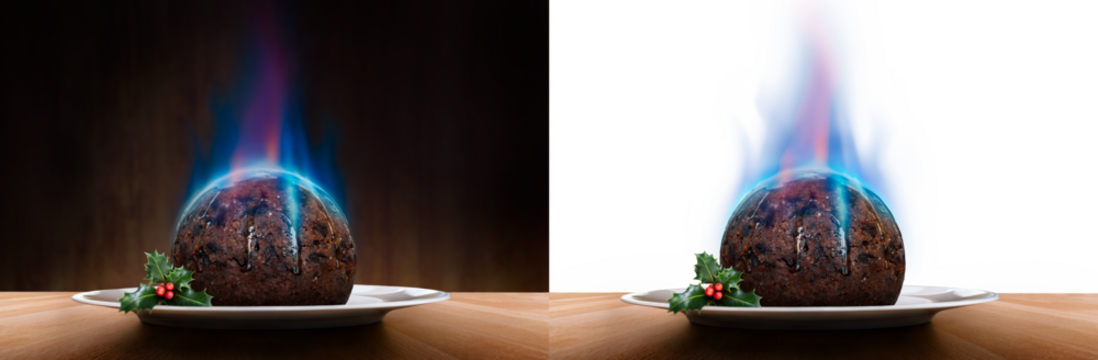 A level view of a traditional Christmas pudding with a blue flame of lit brandy on a round plate with a sprig of holly, berries on a wooden table isolated against a dark and transparent background