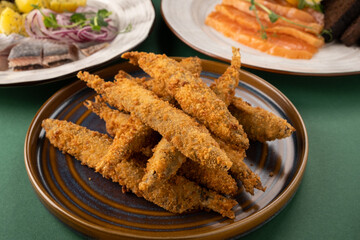 Crispy golden fried fish sticks arranged on a brown plate, surrounded by fresh garnishes and colorful side dishes, showcasing appetizing culinary presentation