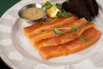 Freshly prepared salmon fillets served on a decorative plate with lemon slices, dark bread, and a small bowl of sauce, showcasing culinary artistry and gourmet presentation