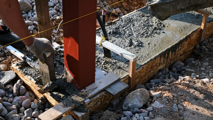 The worker is tamping a wet concrete poured from a mixer truck into a formwork on a construction site. Compaction of the cement mixture. Foundational work. High quality photo.