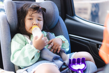 Cute Asian girl drinking milk in a child car seat during a holiday travel trip,The girl is drinking...