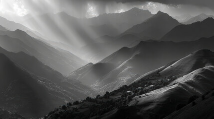 Sunlight piercing through clouds onto layered mountain ranges in a dramatic black and white landscape.