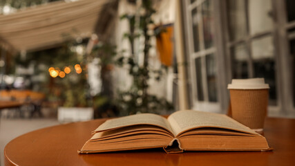 Open book and coffee cup on a table at an outdoor cafe